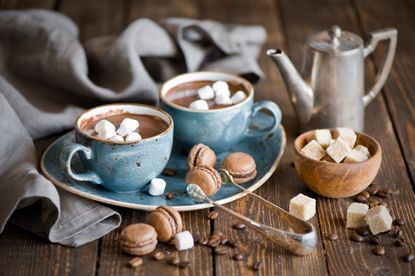 Hot chocolate in mugs with marshmallows, macarons and tea pot