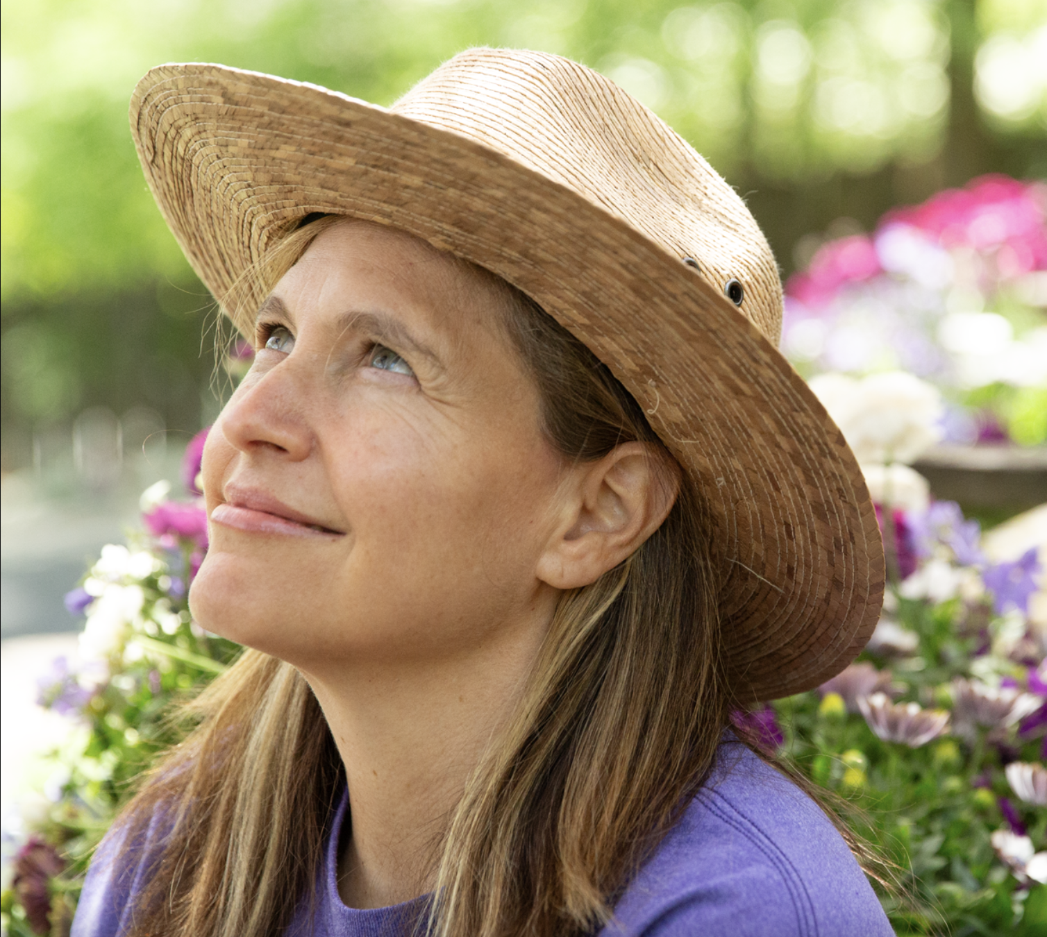 A headshot of a woman wearing a straw hat looking away from the camera