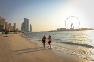 Two men walk down the sand at The Beach, JBR on a hazy evening