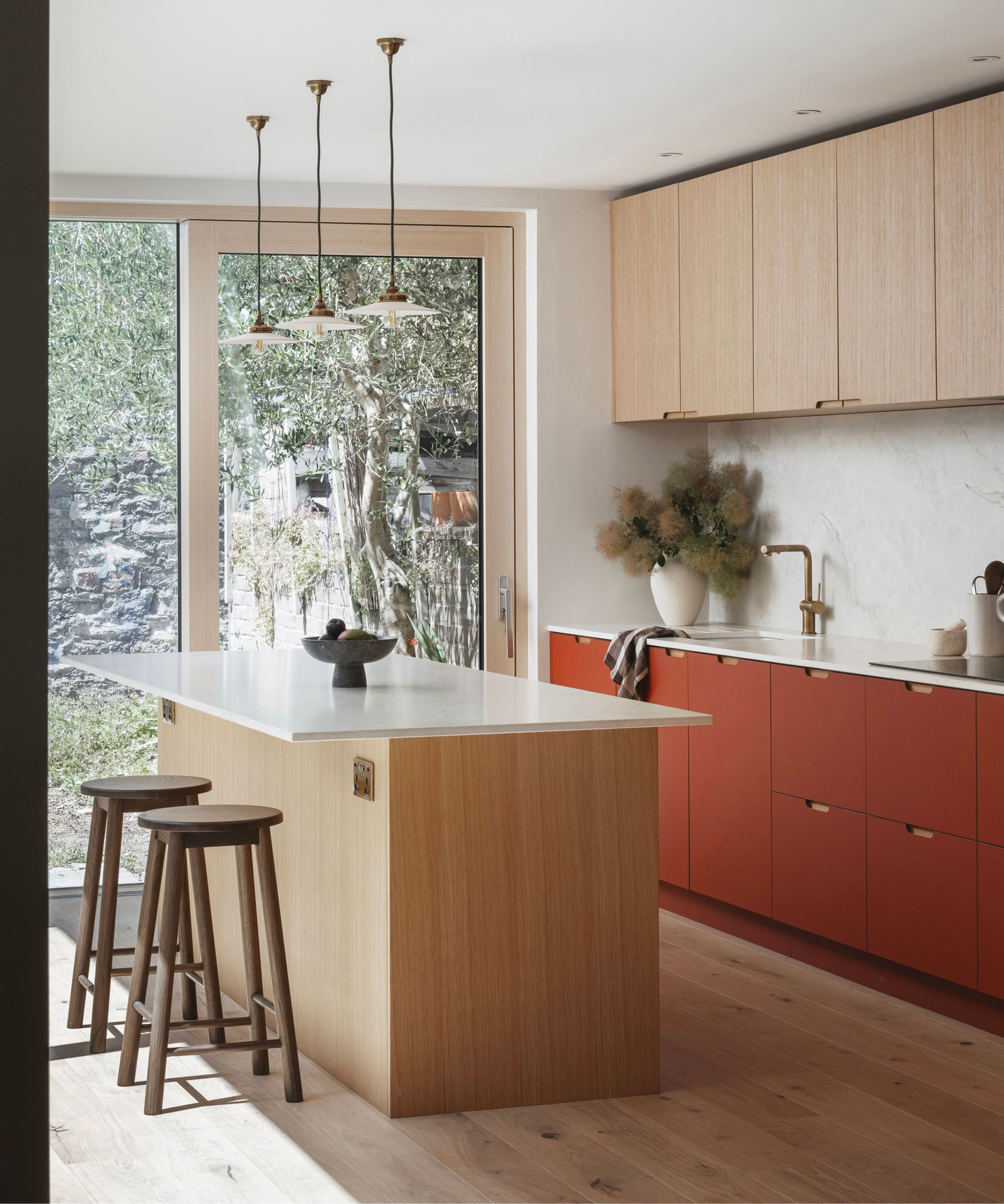 Light-filled modern kitchen with pale wood cabinetry, a white waterfall island, warm wood floors, minimalist pendants, and soft natural textures.