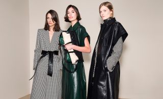 Models wears a longline black and white check coat with a black tie waist. Others wear longline leather coats in black and green.