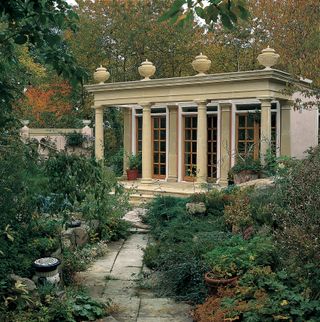 Haddonstone orangery - a vintage looking orangery with columns on the patio, in the middle of an overgrown garden with a stone path