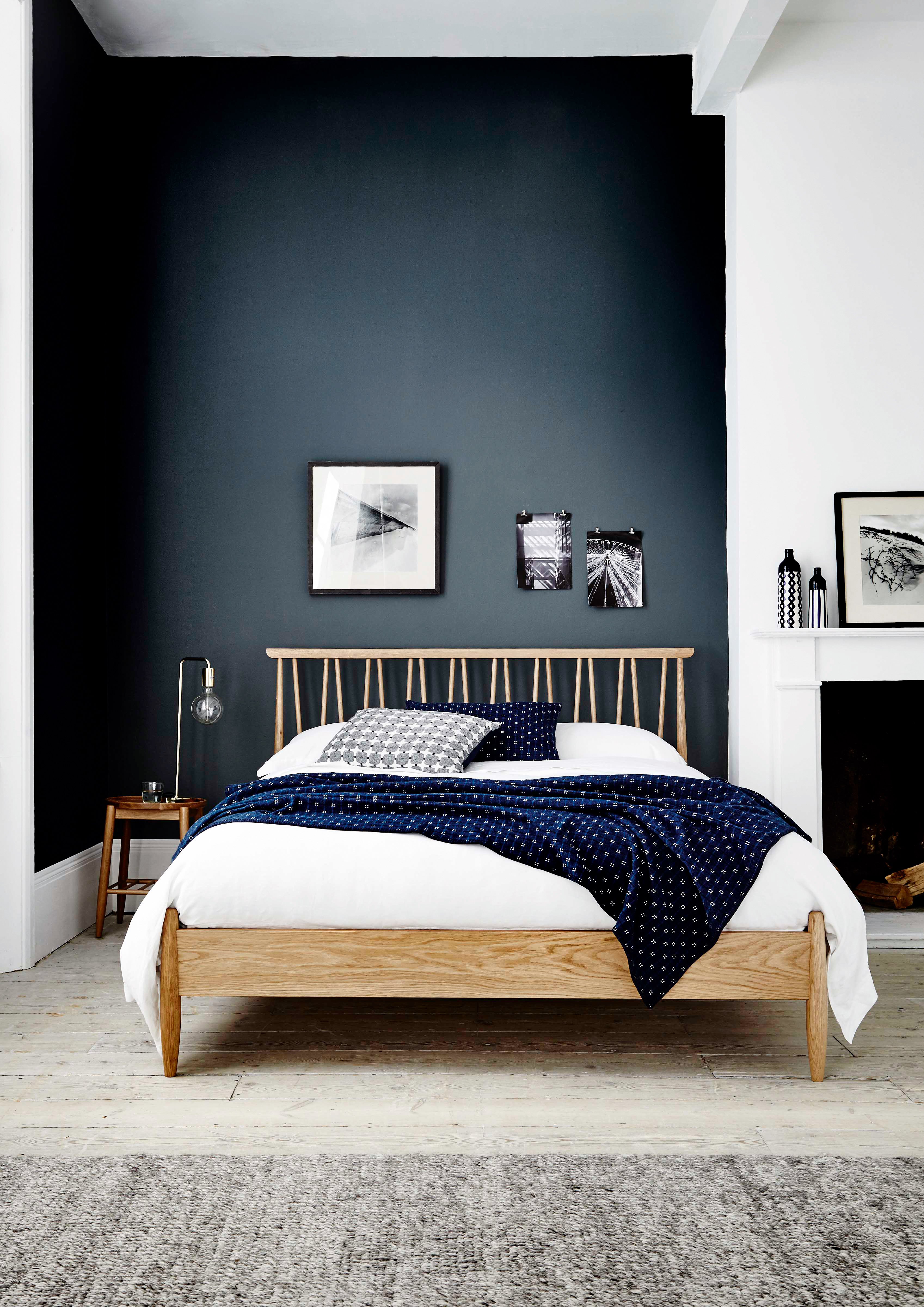 A bedroom with dark blue wall decor, double bed, Edison-style table lamp and grey runner rug