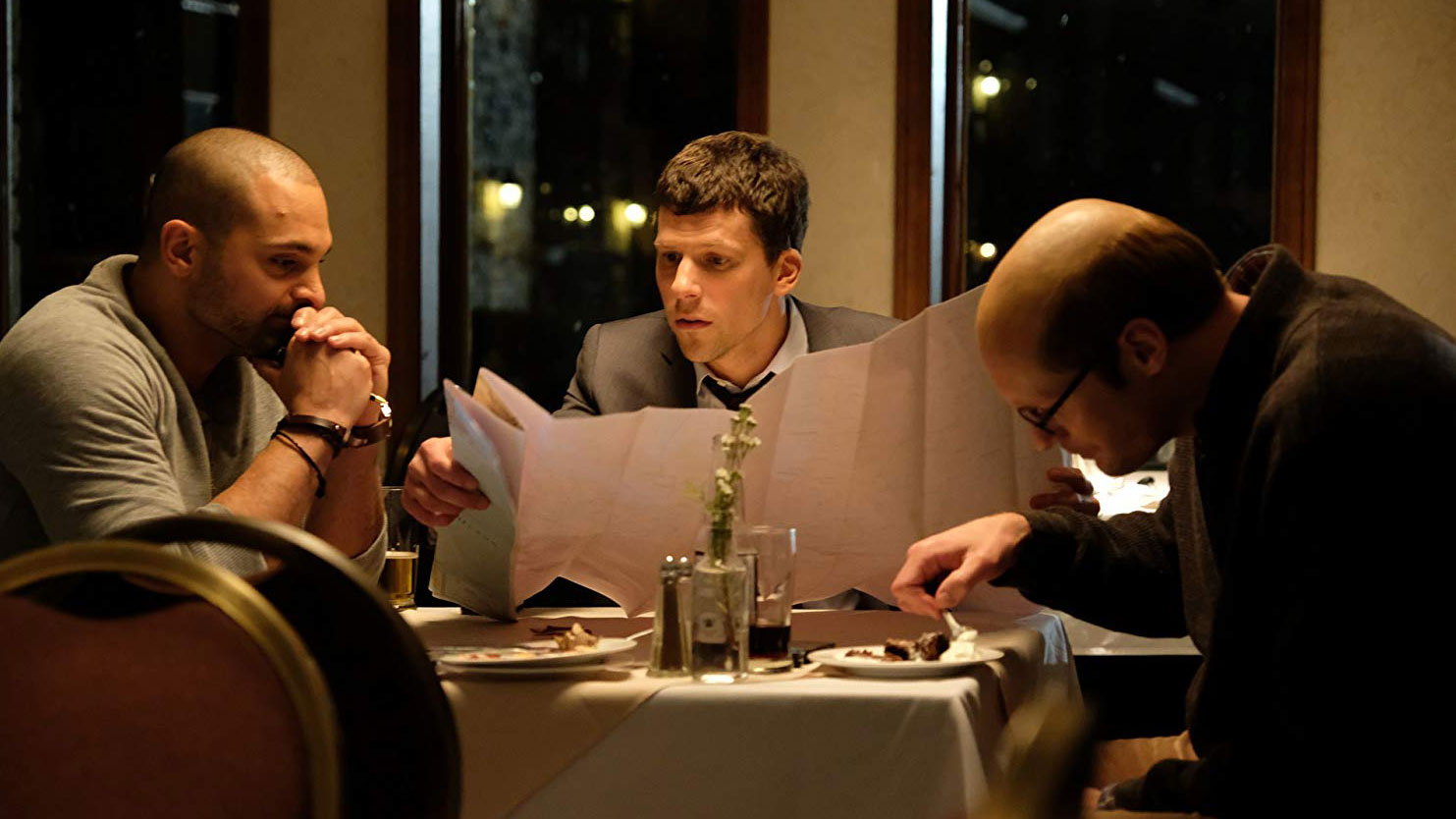 Jesse Eisenberg holds a menu at a restaurant table