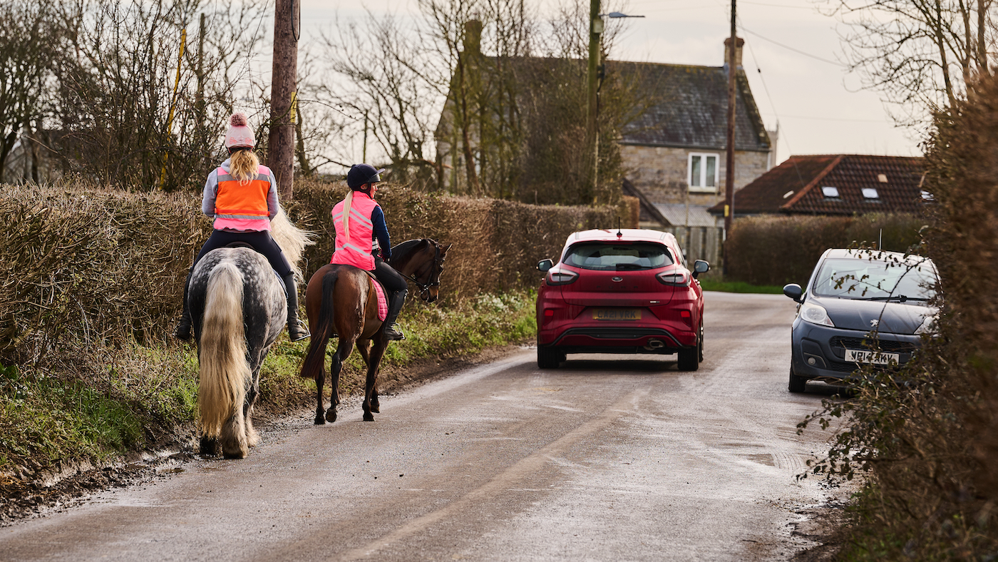 2 horses being ridden on the road.