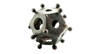 A photo of a metal, baseball-size Roman dodecahedron against a white background.