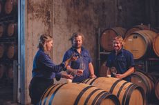 Three people in a wine cellar surrounded by barrels