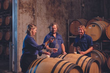 Three people in a wine cellar surrounded by barrels