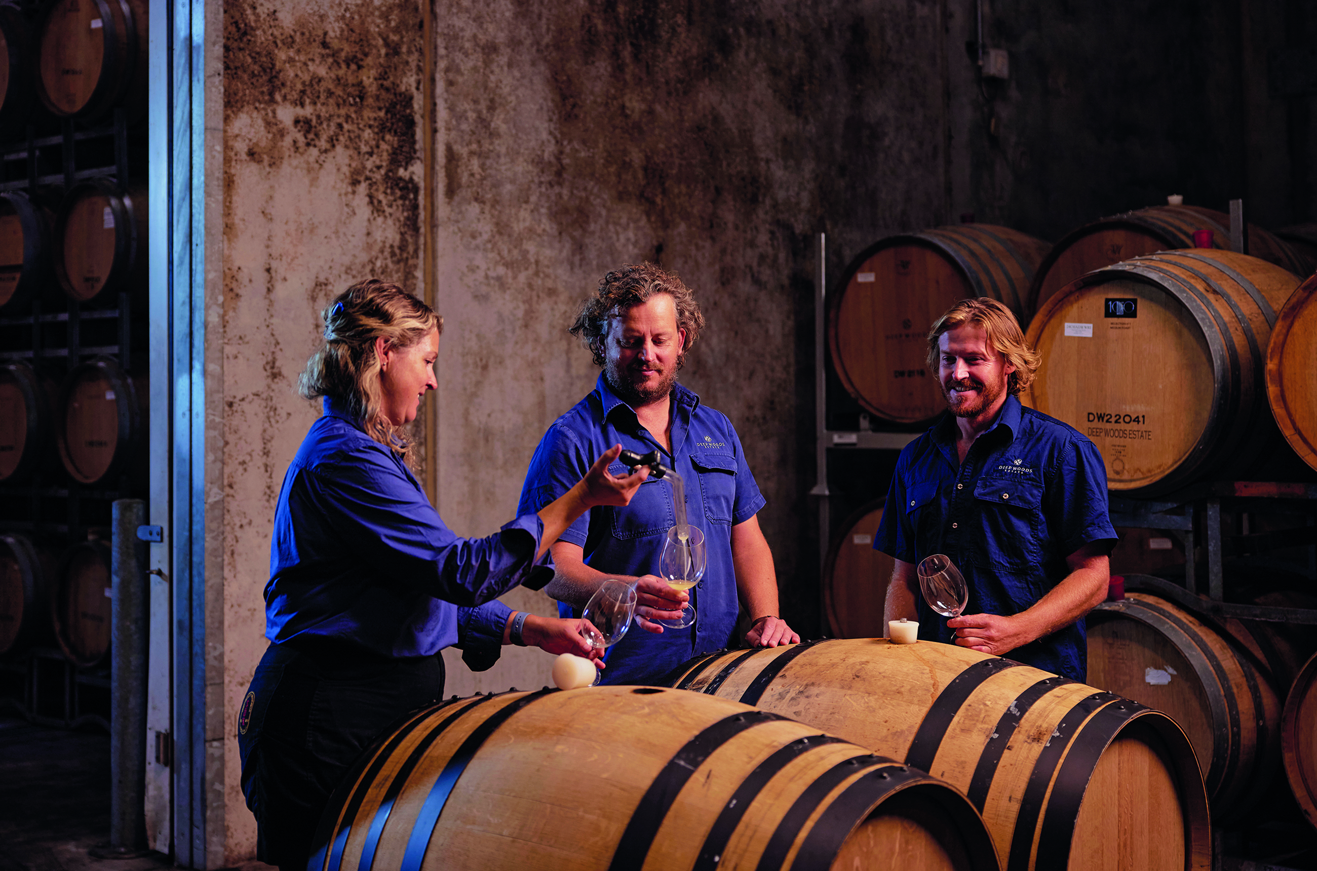 Three people in a wine cellar surrounded by barrels