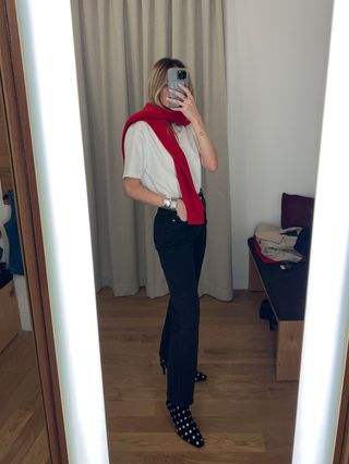 Eliza Huber in the dressing room at Madewell's new SoHo flagship in New York wearing a white T-shirt, black jeans, and studded ankle boots with a red sweater tied around her shoulders.