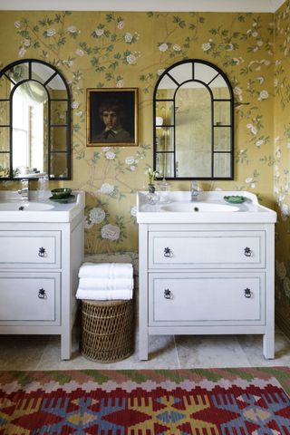 bathroom with yellow floral wallpaper, double vanities, colourful rug