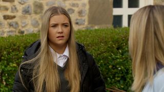 Cathy looking sad and wearing school uniform and coat with her blonde hair long in Emmerdale. 
