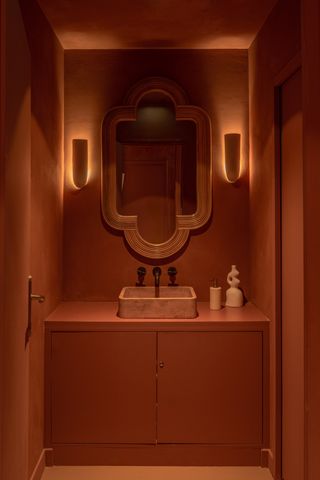 The bathroom of an adobe architecture-inspired restaurant features terracotta decor in ceramics and marble and suffused lighting.