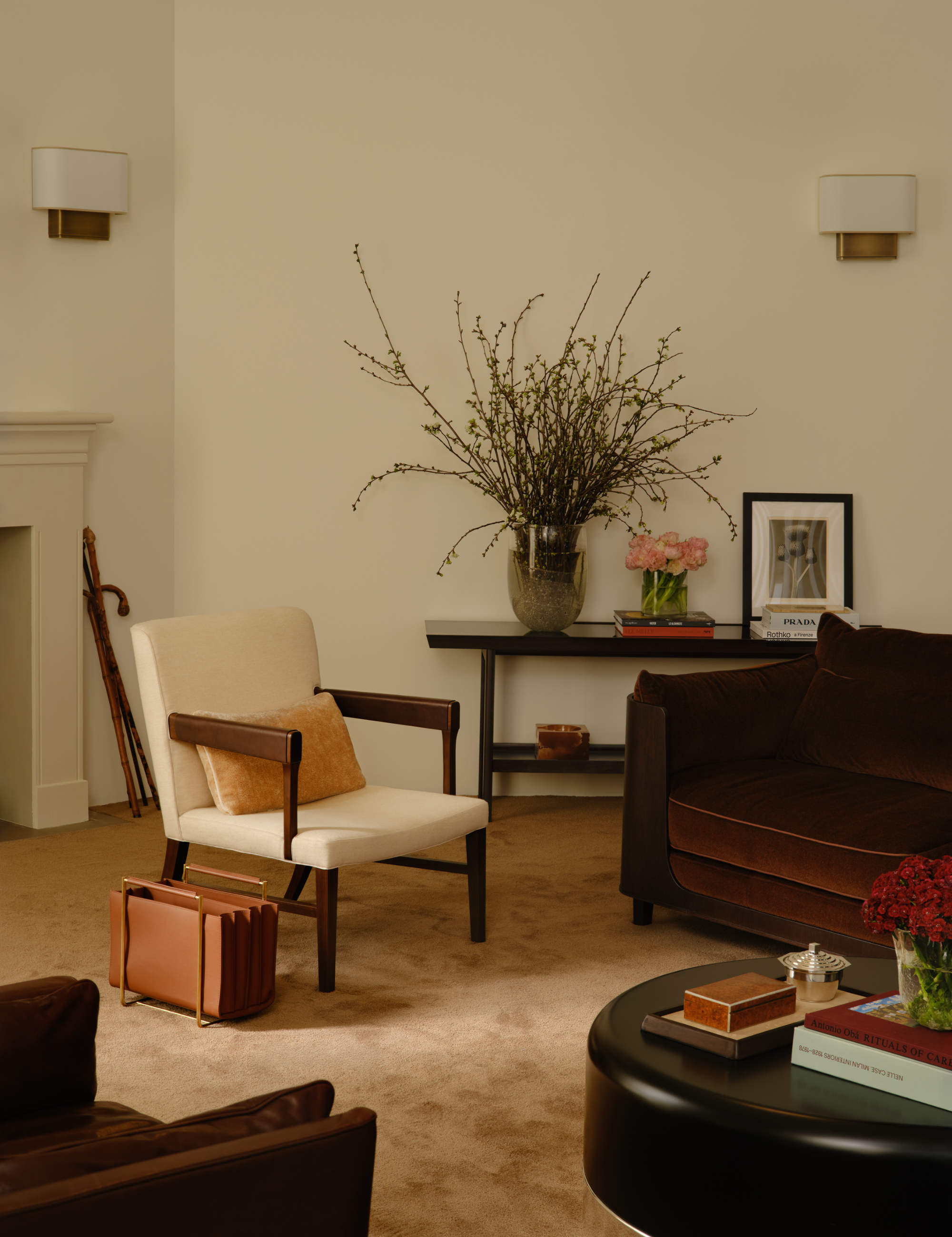 Neutral living room featuring a leather magazine rack, lacquered round coffee table, mid-century-inspired accent chair, and low-slung chocolate sofa.