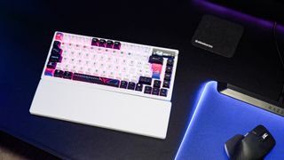An Asus ROG Azoth X gaming keyboard on a desk with wrist rest and lighting enabled.
