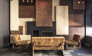 Gaspar, Istanbul, Turkey. A black fireplace surrounded by fury covered sofa and chairs and different sized and coloured wooden planks on the wall around it.