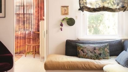 living room with sheer floral roman blinds, a banquette seat with patterned rug, stone coffee table and white floors and walls