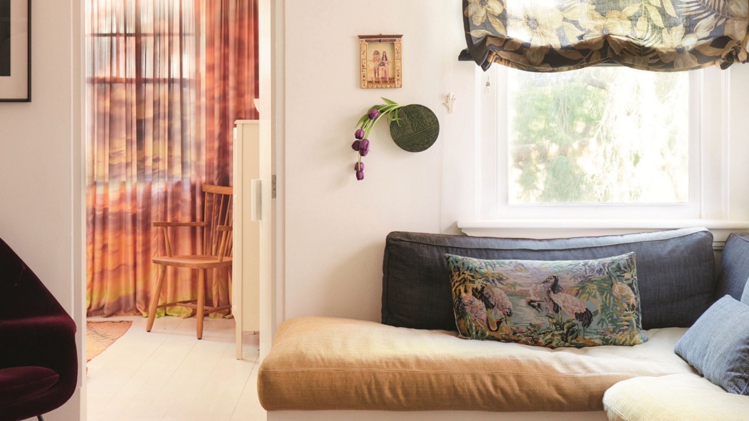 living room with sheer floral roman blinds, a banquette seat with patterned rug, stone coffee table and white floors and walls
