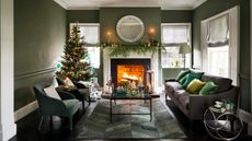 Green living room, open fire, lilac sofa, glass topped coffee table, velvet armchairs, rug, Christmas tree, presents