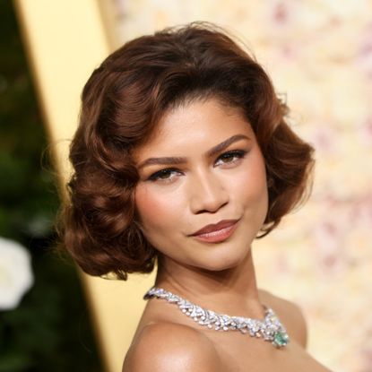 a close up of a light skinned woman with short hair posing in front of a floral background