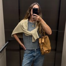 Angie wears a grey t-shirt, cream jumper, blue jeans