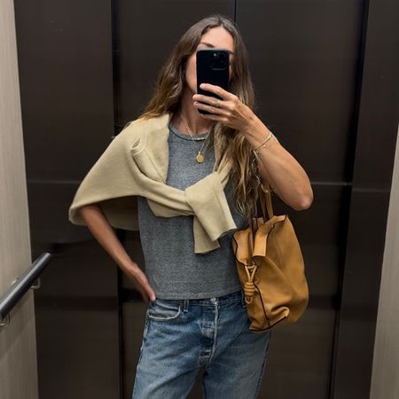 Angie wears a grey t-shirt, cream jumper, blue jeans