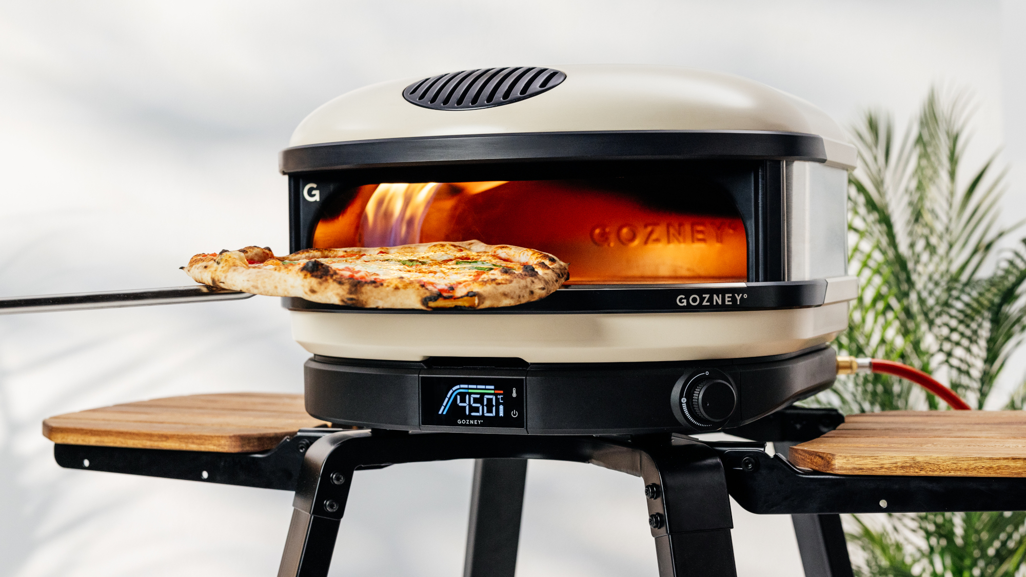 Gozney Arc pizza oven on a table with flames inside and a pizza being removed