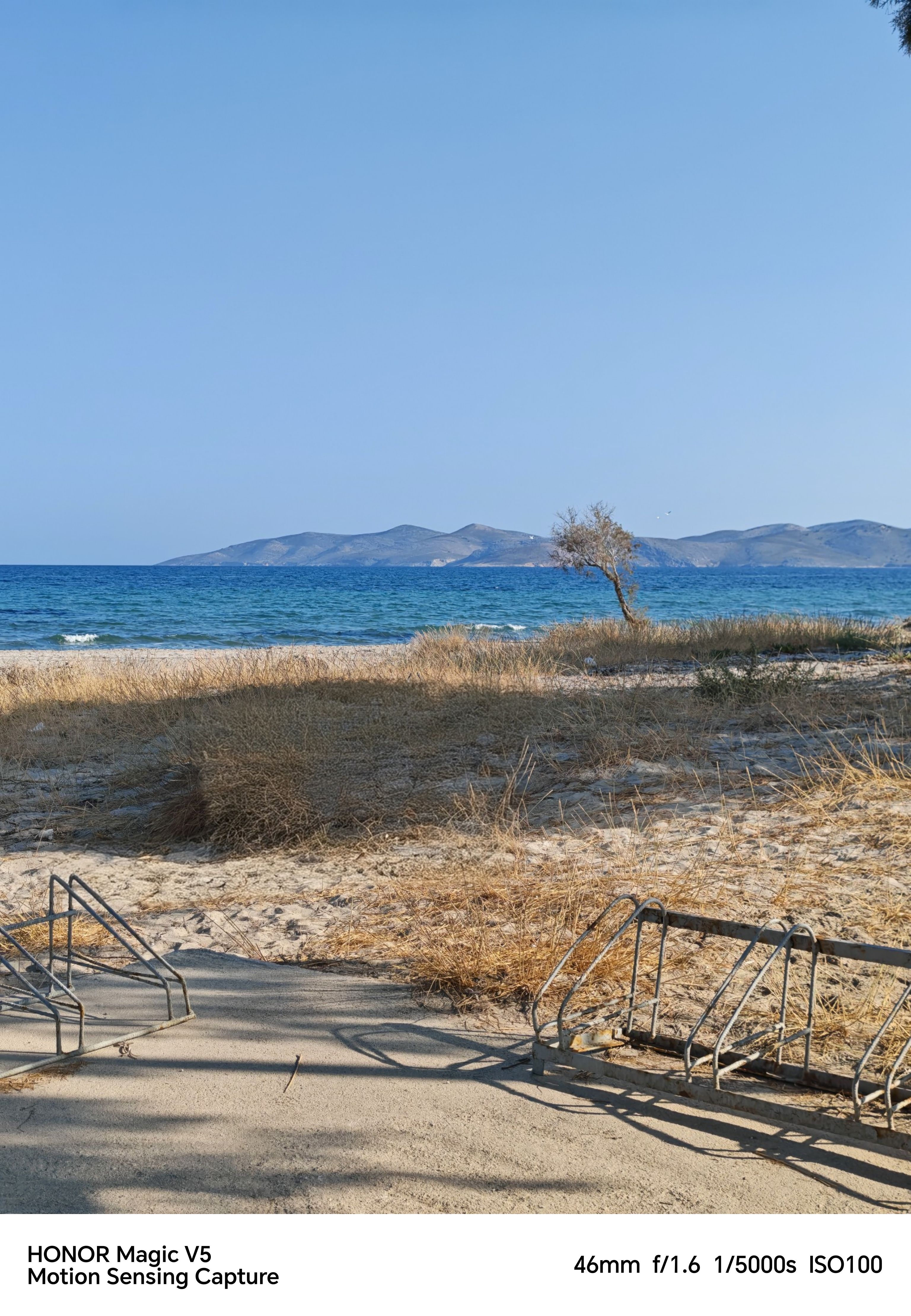 Sandy beach in front of the ocean with mountains and blue sky in the background