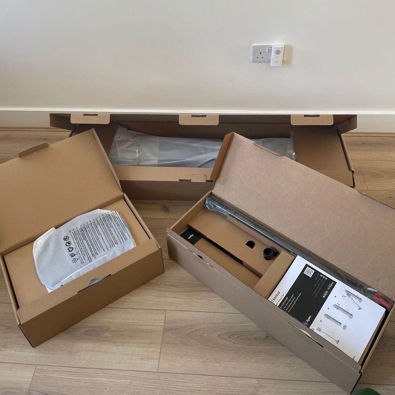 Dyson V10 Konical Cordless Vacuum and Auto-Empty Dok boxes for the smaller components laid out on wood-effect flooring in front of a white wall