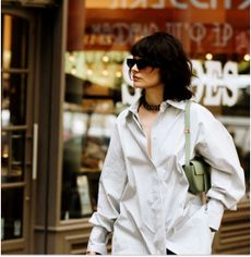 Woman walking down the street in a button-down and a green shoulder bag. 