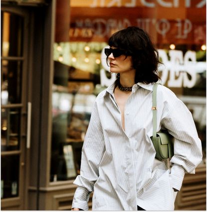 Woman walking down the street in a button-down and a green shoulder bag. 