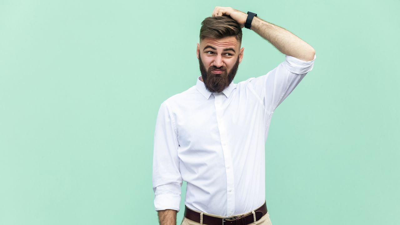 A man scratches his head, looking unsure.