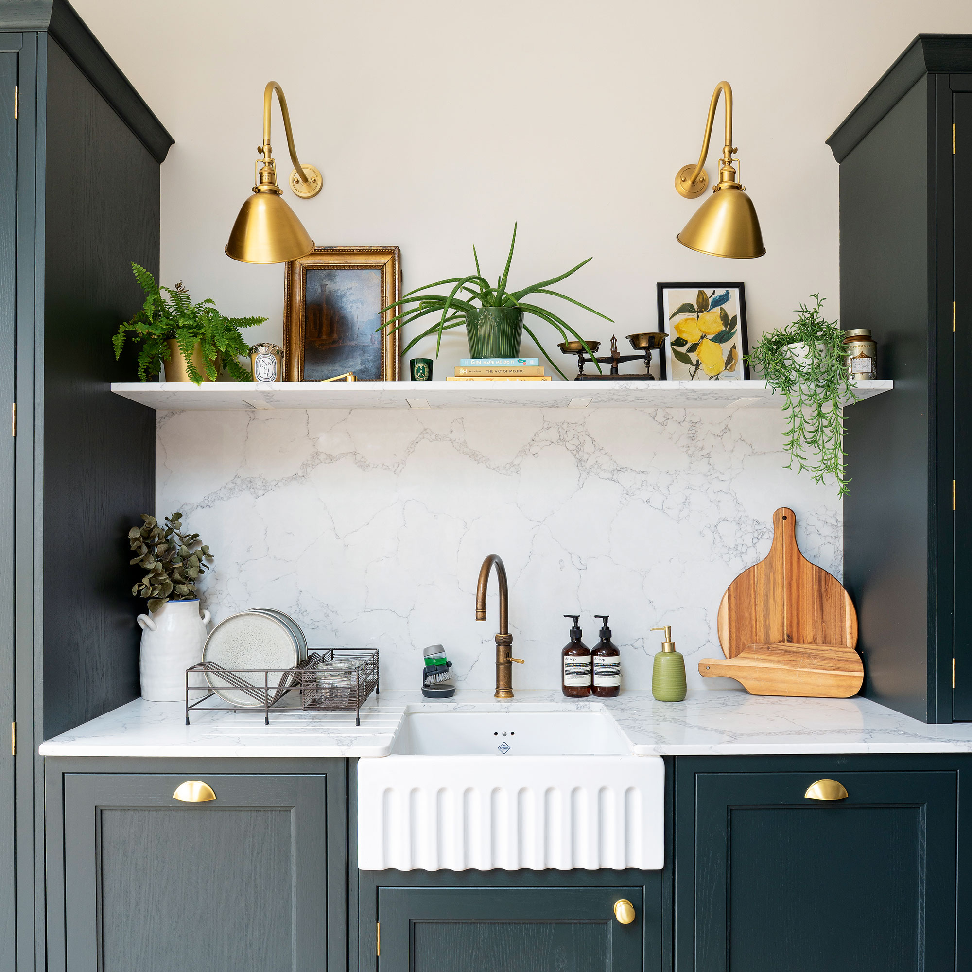 White kitchen sink with gold wall lights, marble worktops and black cabinets