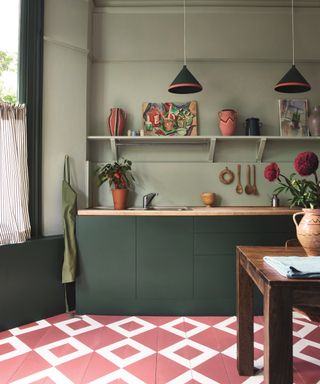 Green kitchen with dark green cabinets, pale green walls, pink and white painted floor, table, open shelving,