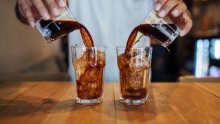 two glasses of iced coffee being poured next to each other, simultaneously