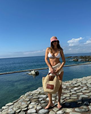 Woman in a swimsuit wearing a woven hat and carrying a woven tote bag.