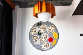 White wall, black curtain, wooden ceiling light with large white bulb shade, grey merble effect ceiling, circular grey based colourful textile artwork on the wall