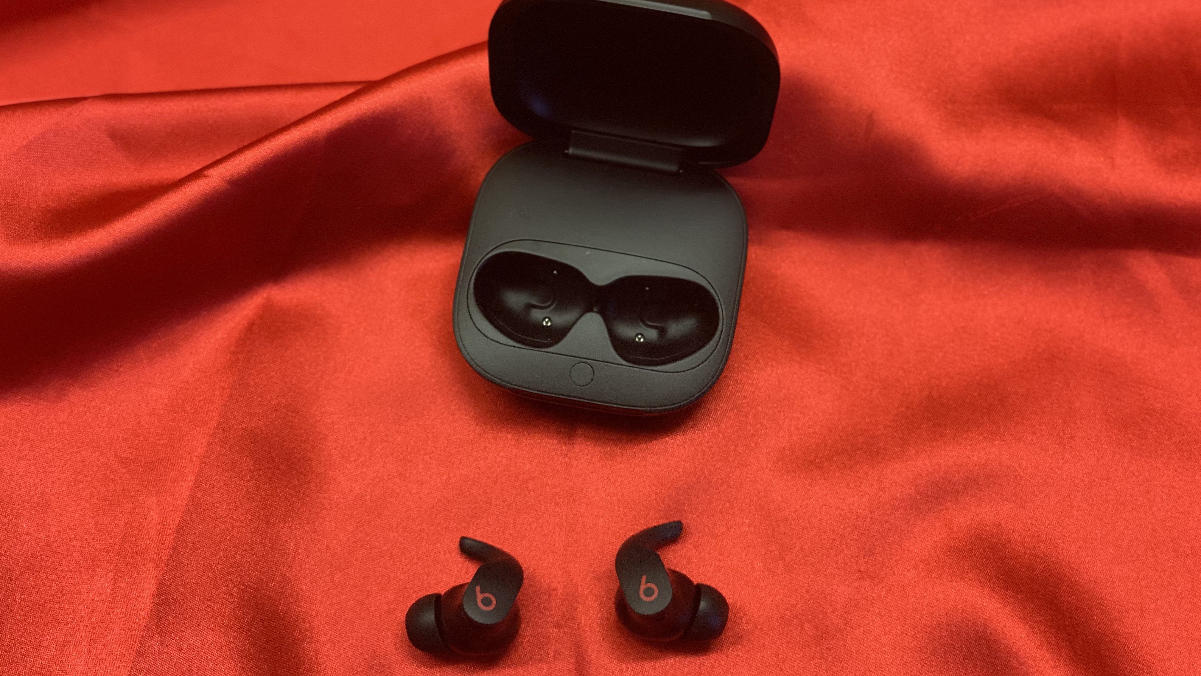 The Beats Fit Pro earbuds next to their charging case on a red backdrop
