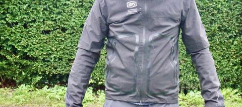 Torso of man wearing black cycling jacket in front of hedge