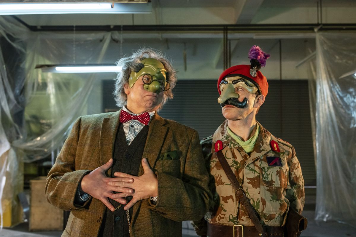 Steve Pemberton and Reece Shearsmith in character as The Doctor and Scaramouche in &#039;Wuthering Heist&#039;. The Doctor wears a tweed jacket, a checked shirt, a red bow tie, a waistcoat and a green mask over the top half of his face. Scaramouche wears an army uniform with a red beret, and a green mask with a large nose over the top half of his face. 