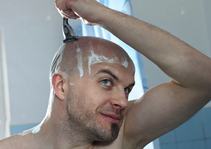 man shaving his head in the shower