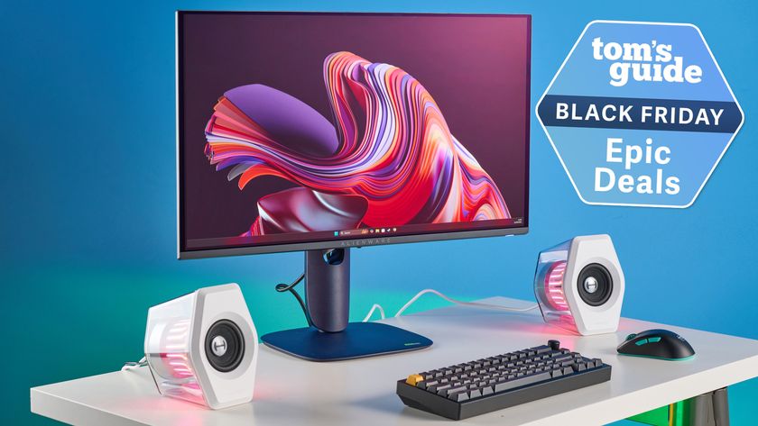 An image of an Alienware Monitor as part of a slick gaming set up, with a blue background and green/pink RGB lighting visible throughout.