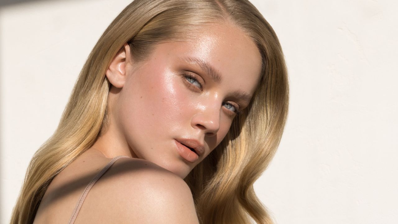 A white woman with blonde hair, bronzed skin, and blue eyes stares into the camera in a close-up image.