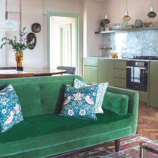 Open plan green kitchen with green velvet sofa.