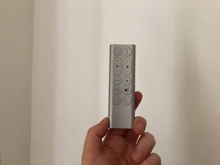 a hand holding the DYSON PURE HOT + COLD FAN remote against a white wall