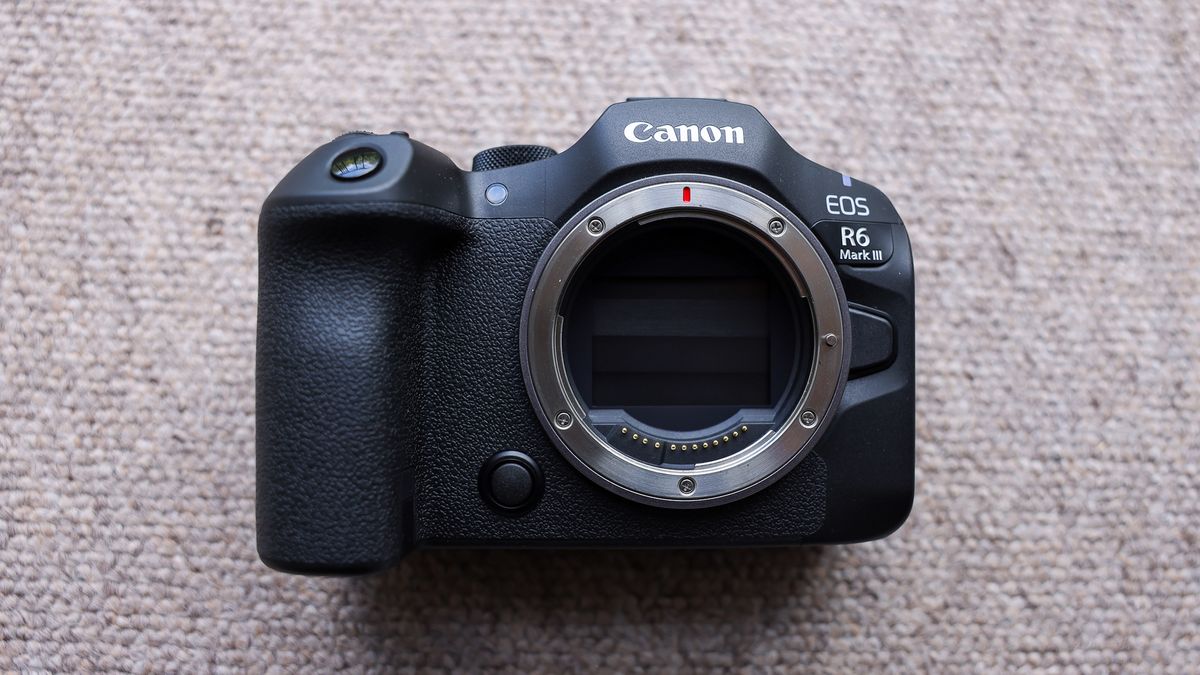The front of the Canon EOS R6 III without a lens on a brown carpet.