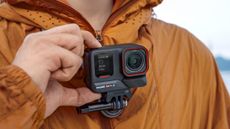 Person in orange jacket pressing button of the Insta360 Ace Pro 2 which is attached to chest harness