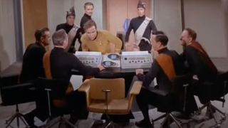 Captain Kirk looking over a computer with lots of other officials