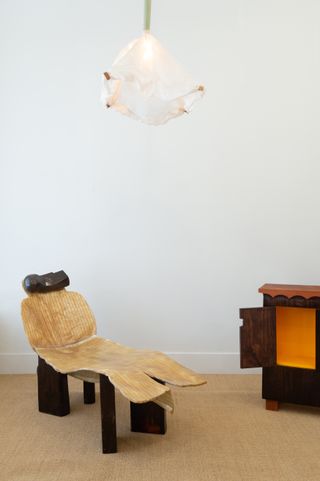 Lounge chair, ceiling lamp with white shade and visible in a corner is a dark wooden cabinet with orange interior