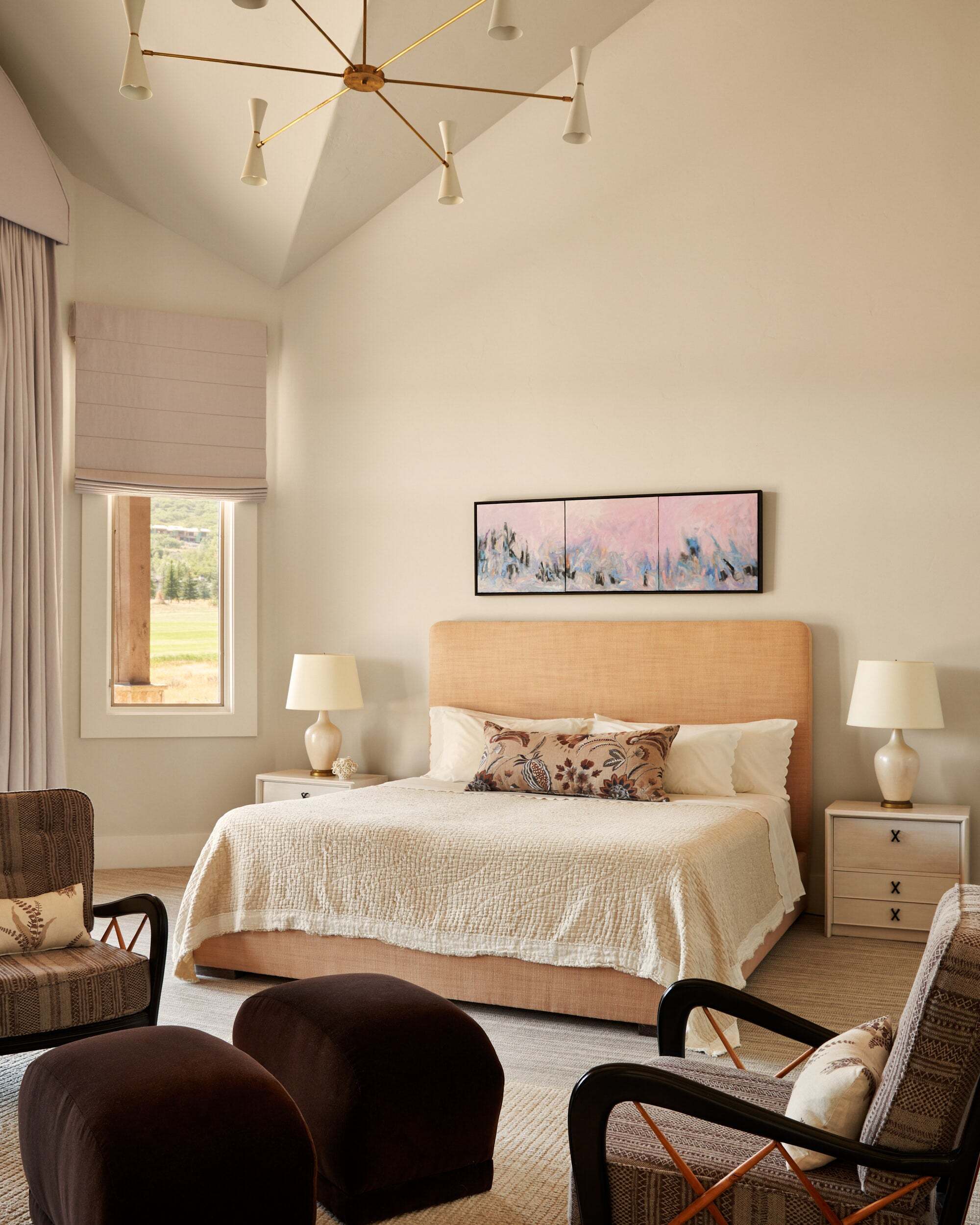 sloped ceiling with white walls, orange bed with art above, bedside tables, two armchairs with two brown ottomans, and a pendant light